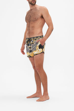 Side view of model wearing Hotel Franks by CAMILLA mens black swim shorts in Tether Me Not print