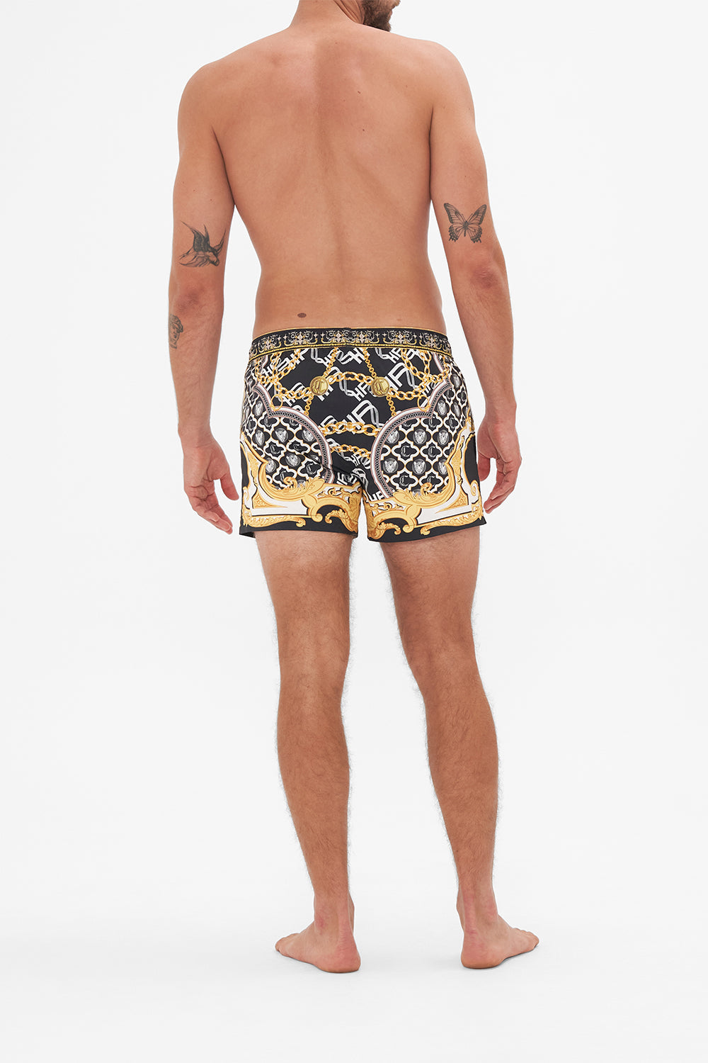 Back view of model wearing Hotel Franks by CAMILLA mens black swim shorts in Tether Me Not print