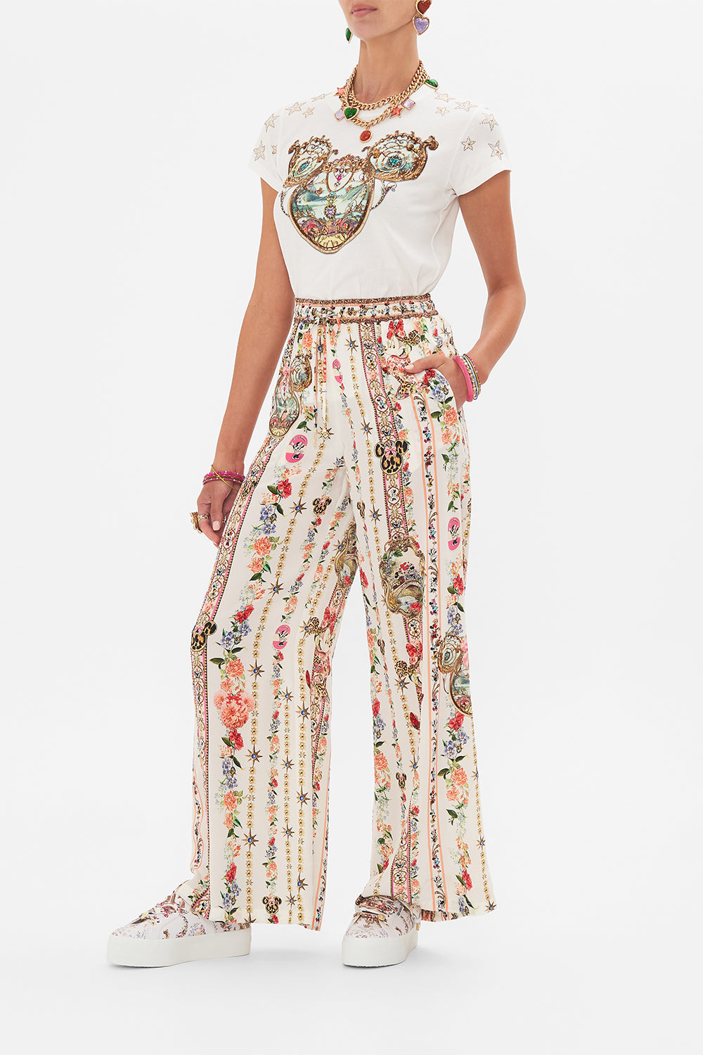 Side view of model wearing Disney x CAMILLA silk pants in Minnie Magic Forever print