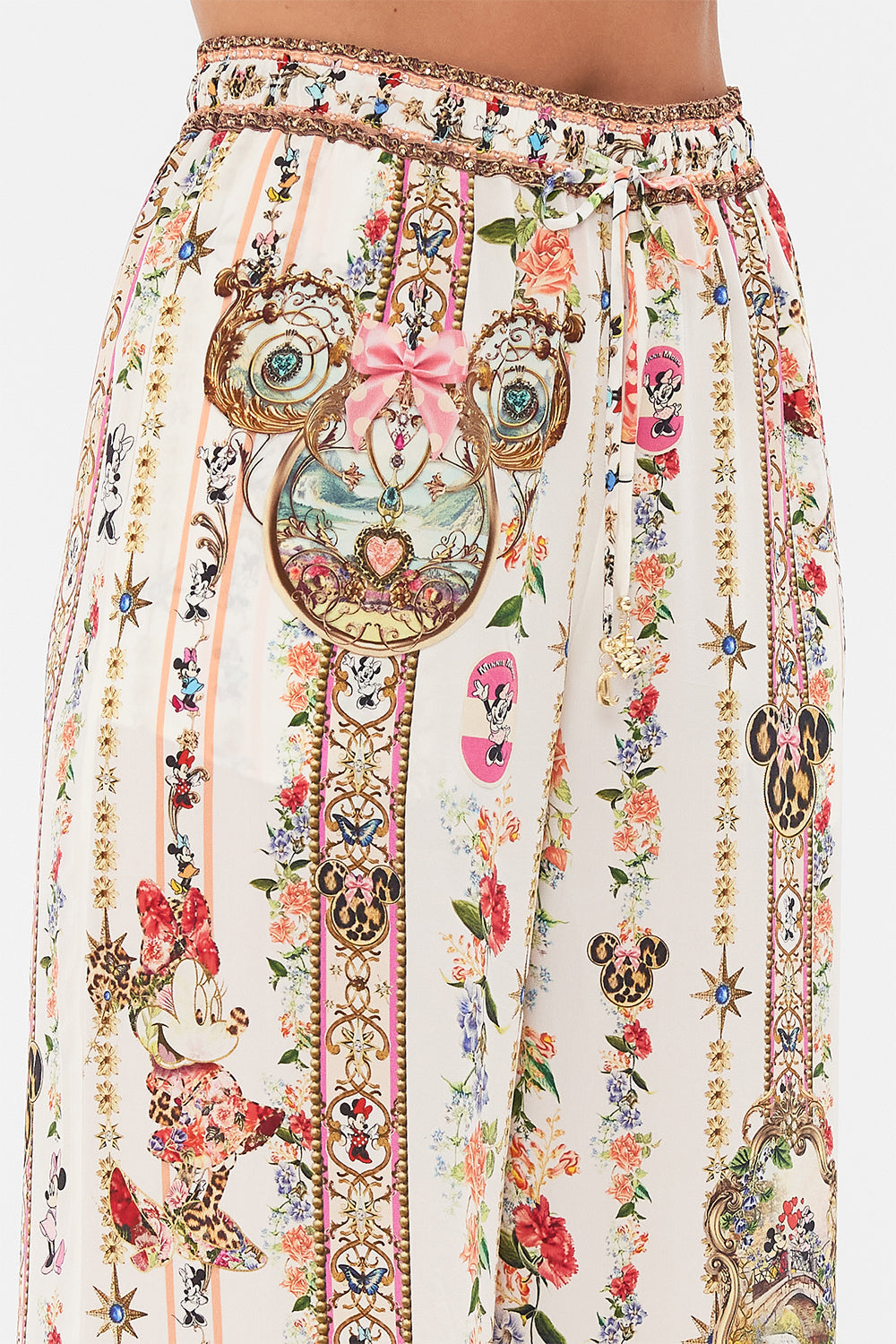 Detail view of model wearing Disney x CAMILLA silk pants in Minnie Magic Forever print